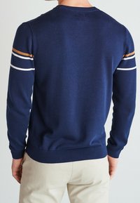 Marineblauer Strickpullover mit Rundhalsausschnitt, ausgestattet mit orangefarbenen, weißen und marineblauen Streifen an den Ärmeln sowie gerippten Bündchen und Saum.