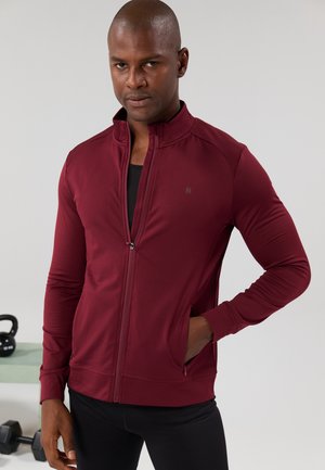 Bordeaux kleurige zip-up jas van rekbaar materiaal, met een hoge kraag en zijzakken. Gladde textuur met een strakke pasvorm.