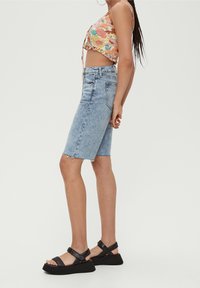 Top recortado floral ligeramente estampado con tirantes finos; shorts vaqueros de talle alto con dobladillo deshilachado; sandalias negras gruesas con suelas gruesas.