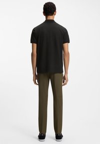 Schwarzes Polohemd mit Struktur und kurzen Ärmeln, kombiniert mit olivgrünen, zulaufenden Hosen und schwarzen Sneakers, Ansicht von hinten.