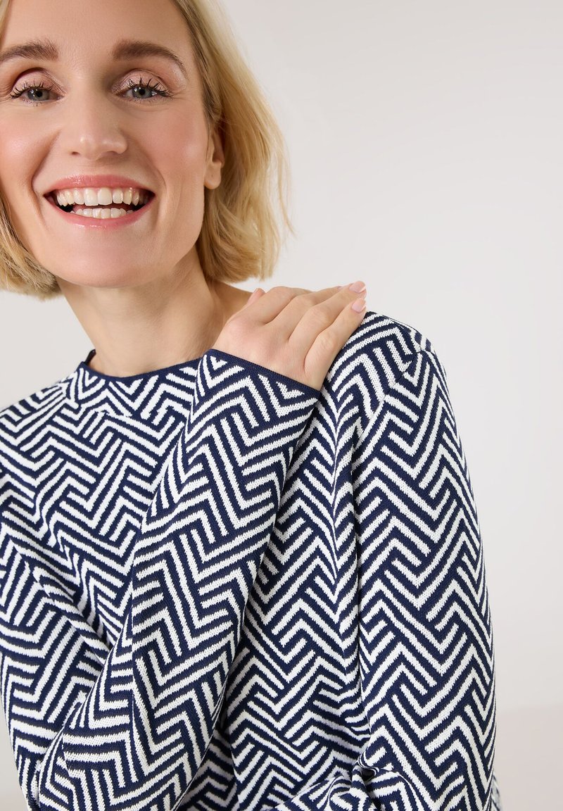Suéter de rayas en zigzag en azul marino y blanco con cuello redondo y mangas largas; hecho de un tejido de punto texturizado. Acabado con un ribete sólido.
