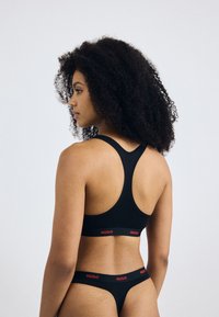 Svart trenings-BH og matchende truse med racerback-design. De elastiske båndene har røde "HUGO"-bokstaver for kontrast. Glatt teksturt.