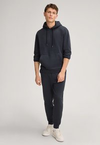 Felpa con cappuccio blu scuro, dotata di tasca frontale, cappuccio con cordini e pantaloni coordinati. Tessuto morbido, vestibilità casual, completata da sneaker bianche.