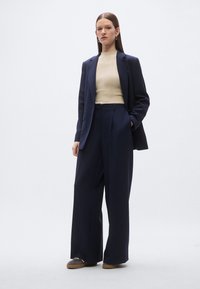 Navy blazer and wide-leg trousers paired with a ribbed beige top. Soft fabric, relaxed fit, side pockets, and minimalistic design.