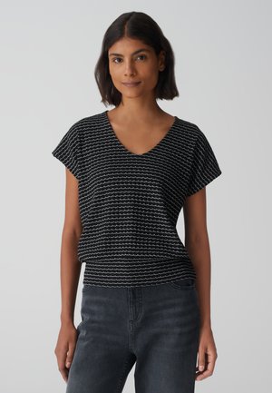 Top nero a maniche corte con scollo a V, caratterizzato da un motivo a onde testurizzato in bianco. Abbinato a jeans grigio scuro, con una vestibilità morbida.