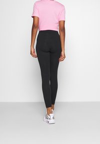 Svarta högmidjade leggings i stretchmaterial, i kombination med en rosa kortärmad t-shirt och vita sneakers. Slät, åtsittande design.