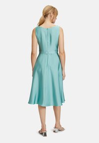 Aqua Satin Kleid mit ausgestellt Rock, ärmellosem Design, Reißverschluss hinten und passendem Gürtel. Getragen mit silbernen High Heel Sandalen.