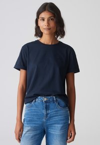 T-shirt di cotone blu navy con collo a giro e maniche corte arrotolate, abbinata a jeans in denim azzurro chiaro con chiusura a bottoni e tasche.