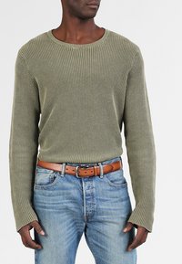 Suéter de punto verde oliva con cuello redondo y mangas largas, combinado con jeans de mezclilla azul claro y un cinturón de cuero marrón.
