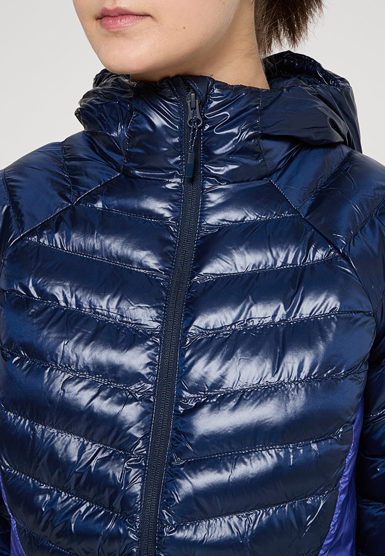 Veste rembourrée bleu marine à finition brillante, avec une fermeture éclair, un col haut et un design matelassé à motifs sur le torse.