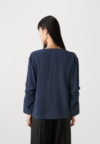 Navy blue long-sleeve shirt with a square neckline, featuring a textured fabric and relaxed fit, displayed from the back.