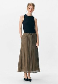 Top negro sin mangas combinado con una falda larga marrón con plisados, que cuenta con una cinturilla elástica y bolsillos, terminando con zapatos negros.
