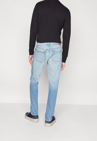 Ljust blå denimjeans med raka ben, med en urtvättad finish, minimal slitage och en beige läderlapp på den bakre midjan.