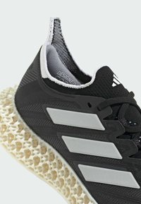 Black athletic shoe with a textured fabric upper, three silver stripes, and a distinctive white lattice midsole. Features a padded collar and laces.