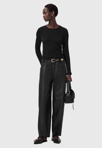 Zwart langshirt gemaakt van textiel, gecombineerd met hoge zwarte leren wijde broek en zwarte schoenen met gouden accent.