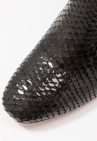 Zapato negro texturizado hecho de material sintético, con un patrón de serpiente brillante y variaciones en el tamaño de las escamas, además de un ligero brillo.