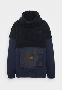 Pullover in pile nero con colletto alto, caratterizzato da un corpo blu navy, polsini elastici e una grande tasca frontale con logo.