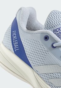 Ljusblå pickleball-sko med ett mesh-överkropp, solida blå accenter, grå detaljer och texturerad sula. Inkluderar snörhål och branding.