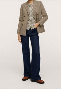 Blazer croisé à carreaux marron porté sur un haut à carreaux, associé à un jean évasé bleu foncé et des bottines marron.