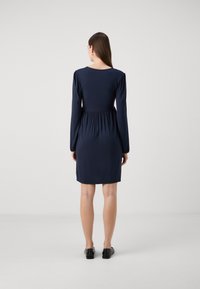 Námořnické modré šaty s dlouhými rukávy, kulatým výstřihem, nabíraným pasem a délkou po kolena. Hladká tkanina s přiléhavým siluetou.