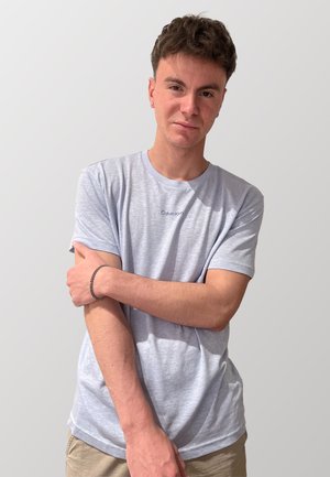 T-shirt grigio chiaro a maniche corte con logo "Calvin Klein", texture morbida, scollatura rotonda, indossato con pantaloni shorts color khaki e bracciale d'argento al polso.