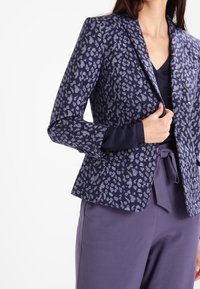 Námornický sako s leopardím vzorem v světlejších odstínech. Má špičatý klopu a strukturovaný střih. Nosené přes tmavý top a kalhoty.