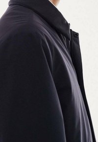 Chaqueta acolchada negra con cuello alto, textura suave, cierre de cremallera y botones a presión en el cuello para mayor calidez y estilo.