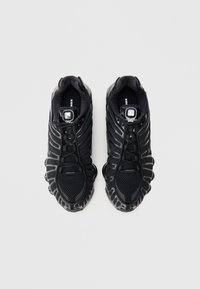 Čierne športové topánky s hornou časťou z sieťoviny, textúrovanými akcentmi, zaoblenou podrážkou a výrazným systémom šnurovania. Na jazyku je umiestnené logo.