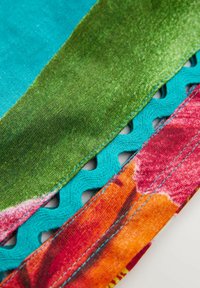 Sezioni di tessuto colorato in teal, verde e arancione con dettagli di cucitura intricati e accenti ritagliati lungo i bordi.
