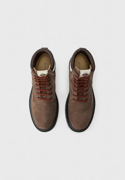 Une paire de bottes en suède marron à lacets avec semelles noires et cols rembourrés, vues de dessus sur un fond blanc.