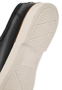Sneaker en cuir noir avec une semelle en caoutchouc blanc. Caractéristiques d'un motif de grip texturé sur la semelle et d'une finition lisse sur le dessus.