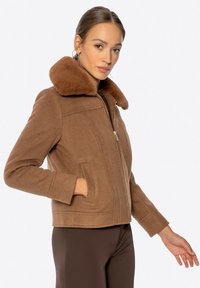 Braune Wolljacke mit einem Kragen aus Kunstfell, Reißverschluss, seitlichen Taschen und einem cropped Design mit gestickten Details auf dem Körper.