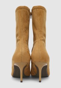 Kamelfarbene Wildleder-Ankelstiefel mit schmalem Stiletto-Absatz, runder Zehenpartie und seitlichem Reißverschluss. Die Nahtdetails auf der Rückseite sorgen für einen eleganten Abschluss.