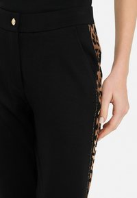 Pantaloni jogging neri con un pannello laterale a stampa leopardata; realizzati in un materiale morbido, presentano un bottone dorato e cuciture decorative lungo il lato.