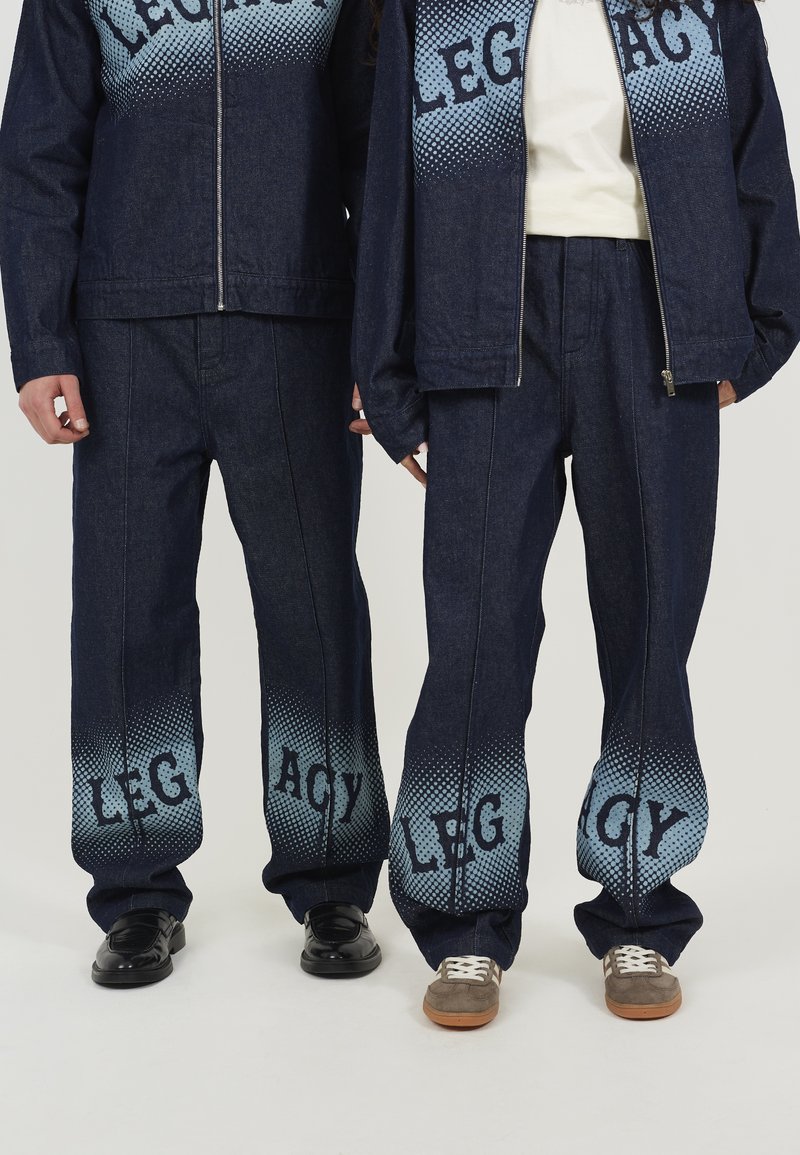 Pantalones y chaqueta de mezclilla oscura con un diseño de degradado azul claro y el texto "LEGACY" en grandes letras en las secciones inferiores.