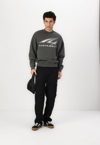 Gray sweatshirt with a graphic logo, paired with black cargo pants. The outfit is complemented by black sneakers with gum soles.