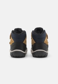 Bruine en marineblauwe enkelboots van suede en synthetische materialen, met klittenbandsluitingen, een zachte voering en gestructureerde zwarte rubberen zolen.