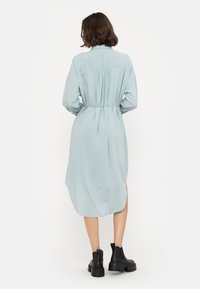 Ljusblå klänning med lång ärm, samlad rygg, skärp i midjan, asymmetrisk fåll, kombinerad med svarta ankelboots.