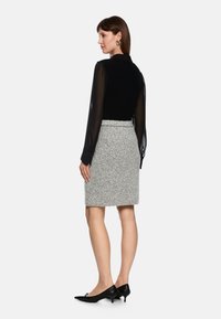 Black knit top with sheer sleeves, paired with a grey textured pencil skirt. Footwear features pointed toe and small heels.