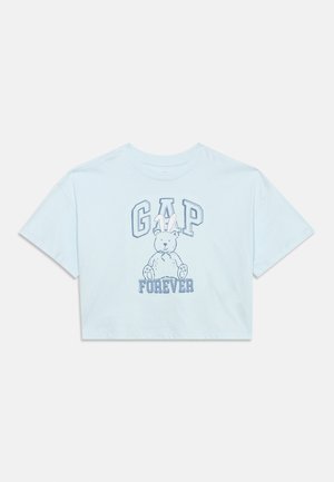T-shirt bleu clair raccourci avec le texte "GAP FOREVER" et un ours en peluche portant des oreilles de lapin imprimé au centre.
