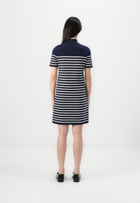 Marineblå stripete kjole med korte ermer, med horisontale hvite striper, polo-krage og rett silhuett. Svarte sko fullfører looken.