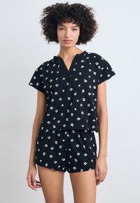 Schwarzes Baumwoll-Pyjama-Set mit kurzen Ärmeln und einem V-Ausschnitt-Oberteil, kombiniert mit passenden Shorts. Beide Teile haben ein mehrfarbiges Muster.