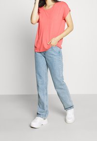 Korallfärgad t-shirt med rullade ärmar, i kombination med ljusblå raka jeans och vita sneakers. Enkelt design med en avslappnad passform.