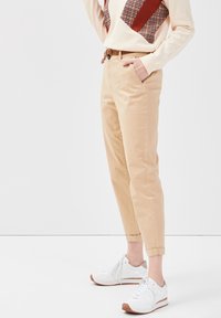 Pantalons en coton khaki avec une coupe fuselée, dotés d'une taille ceinturée et de poignets roulés. Assortis à des baskets blanches avec des accents marron.