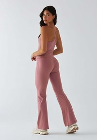 Różowy sportowy top na ramiączkach i spodnie rozszerzane, wykonane z rozciągliwego materiału. Gładka faktura z minimalnymi zdobieniami, w połączeniu z jasnymi trampkami.