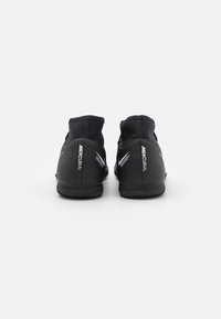 Czarne buty sportowe z teksturowanym wzorem, wysokim kołnierzem oraz wyraźnym logo "Mercurial" po bokach. Płaska podeszwa zapewniająca przyczepność.