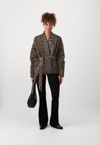 Kimono stylový kabát s leopardím vzorem, se stažitelným pasem, dlouhými rukávy a volným střihem, spárovaný s černými zvonovými kalhotami a černou taškou.