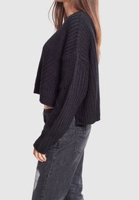 Maglione nero corto con un motivo a maglia testurizzato, caratterizzato da maniche ampie e una vestibilità rilassata, abbinato a jeans neri strappati.