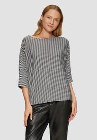 Zwart-wit gestreepte blouse met een bootnek, driekwartmouwen en een losse pasvorm, gecombineerd met zwarte leren broeken.