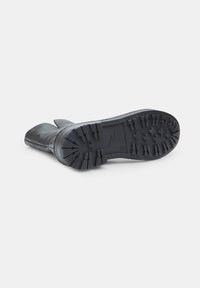 Black leather boot with a textured rubber sole, featuring a tread pattern for grip and a rounded toe design.